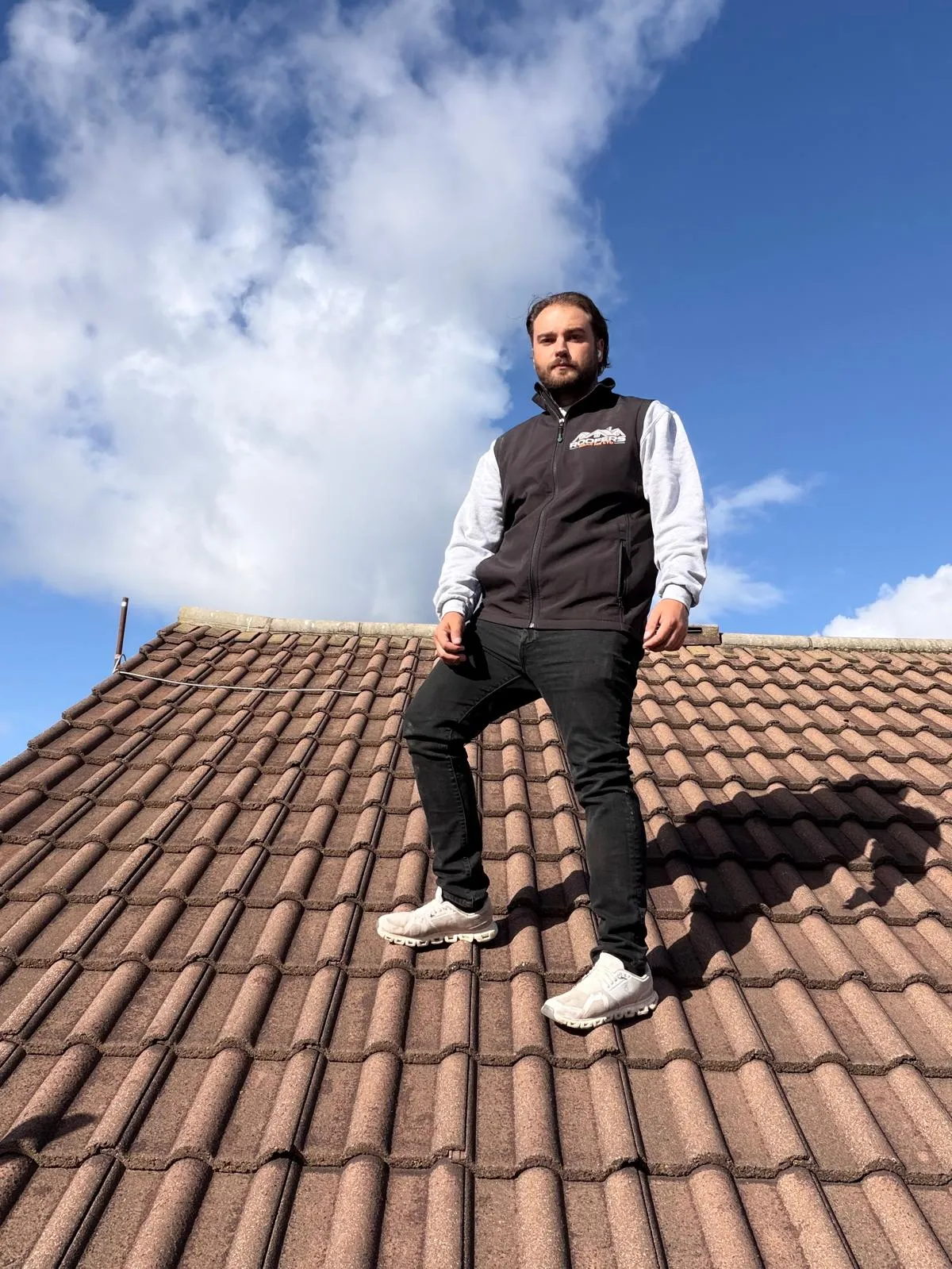 John Jones, owner of Roofers Near Me, standing on a tiled roof in a branded gilet
